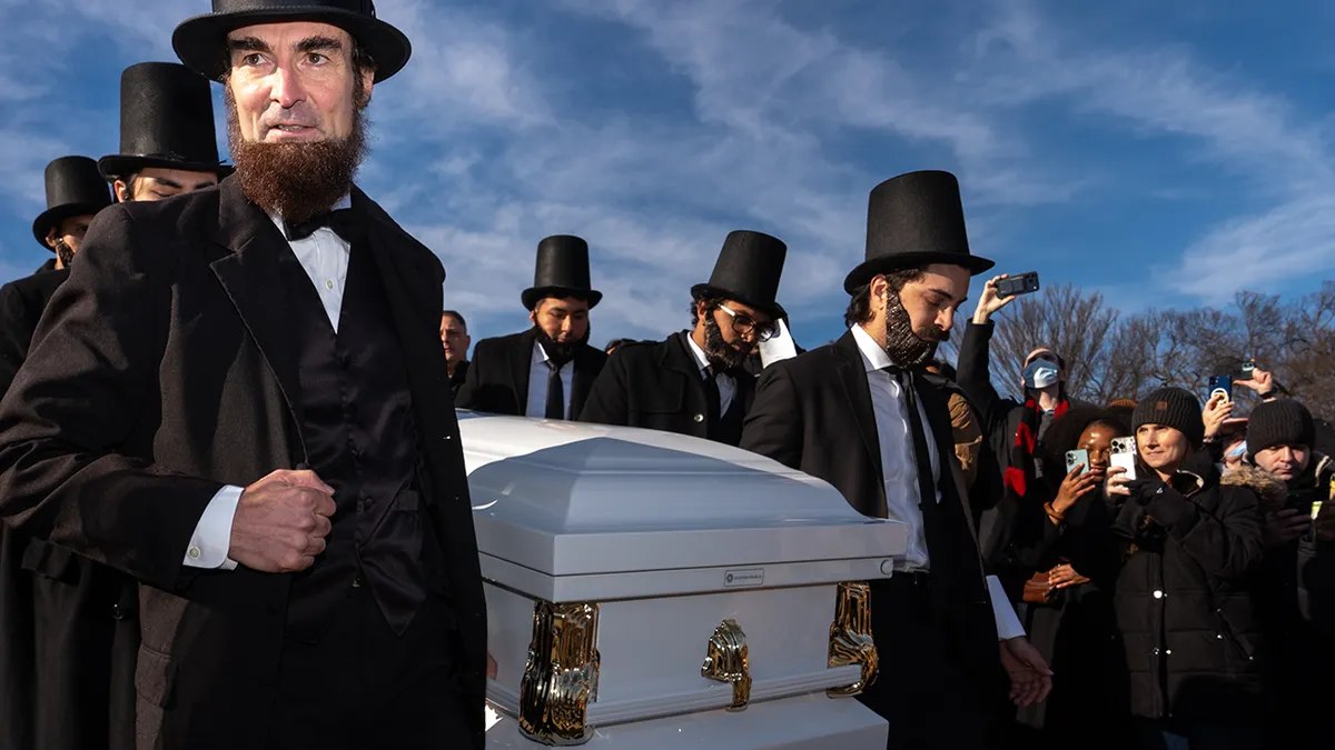 Lincoln impersonators in top hats carrying a casket down the steps of the Lincoln Memorial